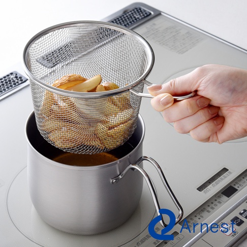 一只手正握著不鏽鋼濾網提籃，籃內裝有炸薯條，提籃置於一個裝有油的不鏽鋼鍋上方，鍋子有兩個金屬把手。