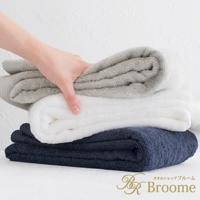 一隻手拿著疊放的三條今治純棉長毛巾，分別為淺灰色、白色和海軍藍，毛巾呈現菱紋質感。