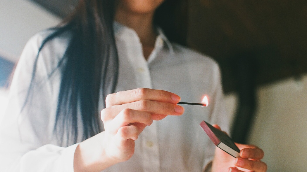 手持一根燃燒的火柴，旁邊是粉紅色的火柴盒。