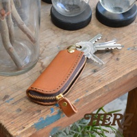 職人手作皮革鑰匙包，咖啡色皮革，附有黃銅拉鍊和掛環，可收納多把鑰匙，展現簡約實用的設計風格。