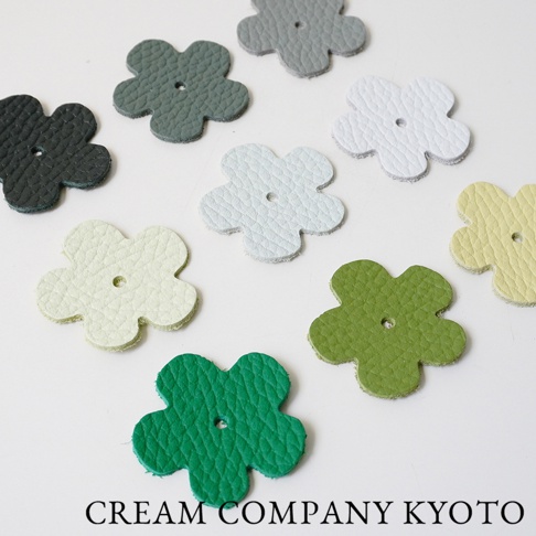 多個皮革製成的五瓣花形狀小飾品，顏色包含黑色、深綠、淺綠、淺藍、白色、米白、淺黃，每朵花中心皆有一個小孔。