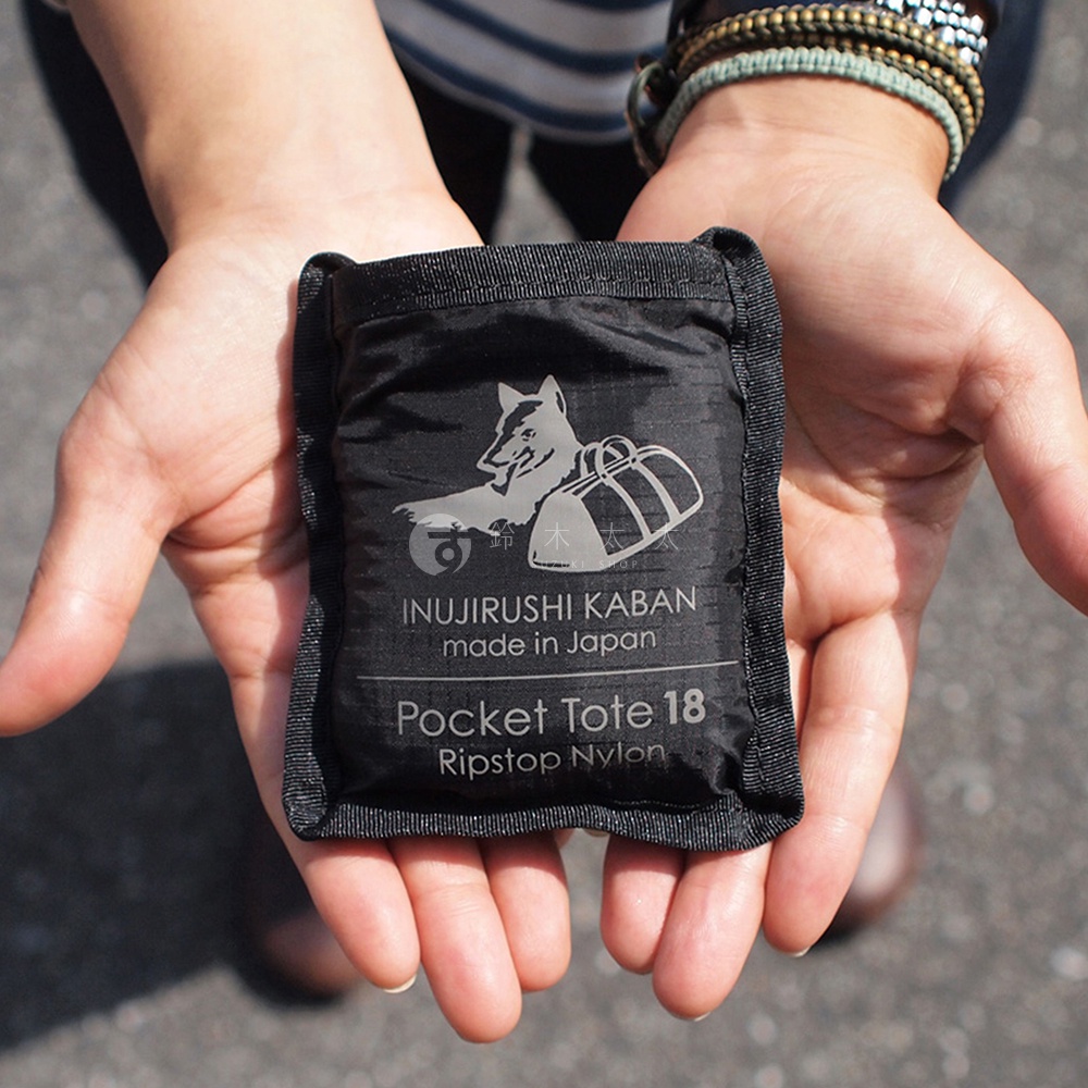 黑色犬印鞄環保折疊收納購物袋，採用 Ripstop Nylon 材質，上面印有狼與行李箱圖案，並標示「INUIRUSHI KABAN made in Japan Pocket Tote 18」。