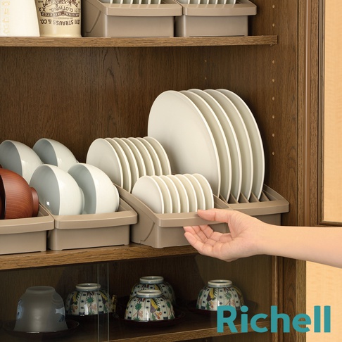 櫥櫃式餐盤收納架上整齊擺放著多個白色盤子和碗，右側有手伸入架中，架下方展示著有花紋的碗盤。