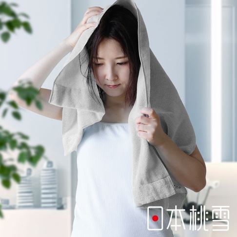 一位女性頭上蓋著一條淺灰色的厚手迷你浴巾，雙手將浴巾固定在頭部。浴巾材質可見細緻的紋理。