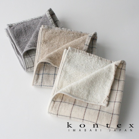 三條折疊的GRAPH草木染格紋有機棉毛巾，顏色由淺至深分別為米白色、淺棕色與灰色。毛巾表面有細緻的格紋圖案，材質觸感柔軟。