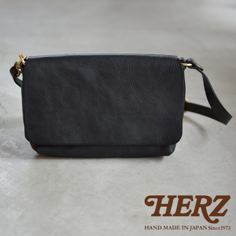 黑色皮革斜背包，有翻蓋設計，配有金屬扣環和可調節背帶。