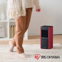 紅色直立式陶瓷電暖器，黑色網狀出風口和控制面板，放置於白色地毯上，旁邊有一位穿著米色毛衣和棕色長褲的人。