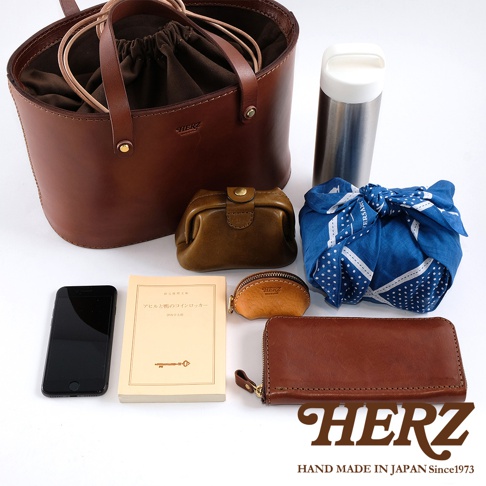 職人手作咖啡色皮革束口手提包，內含深棕色束繩內袋，搭配同色系皮革零錢包、長夾、手機、書籍及藍色印花布包，另有一支銀色保溫瓶。