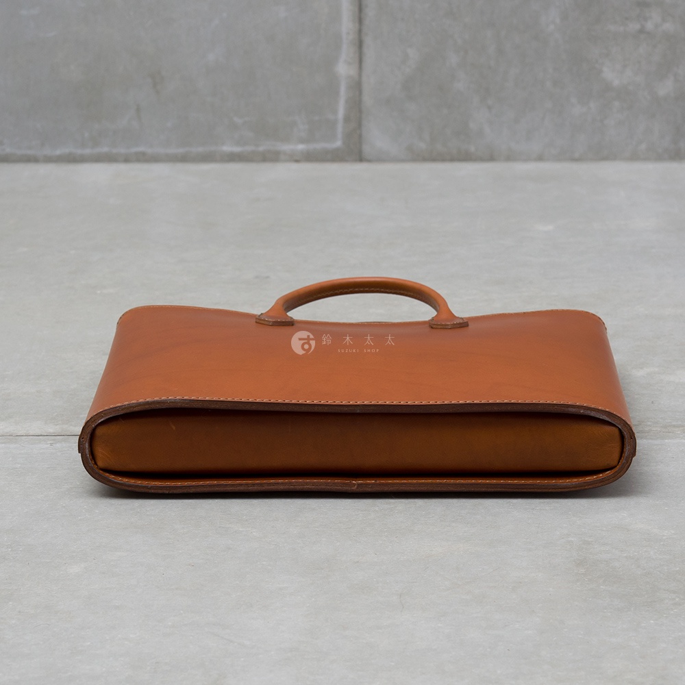 職人手作的淺棕色皮革Organ薄型公事包，設有提把，簡潔俐落的設計，適合商務場合。