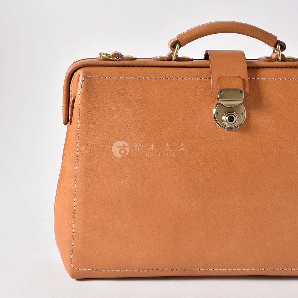 職人手作皮革軟式杜勒斯三用背包，呈現溫潤的咖啡色調，以精細的車縫線勾勒出包款輪廓，搭配復古金屬鎖扣與提把，展現經典的醫生包設計。