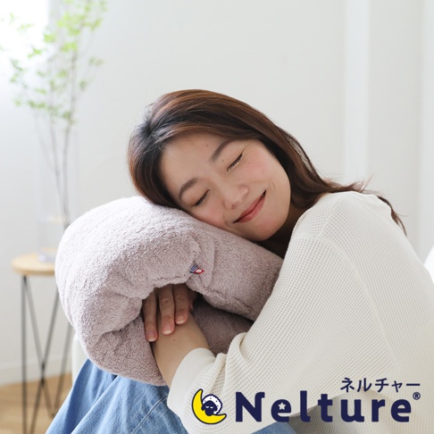 粉色毛圈布材質的甜甜圈形狀枕頭，環繞著一位閉眼微笑的女性。枕頭上有一個小小的美國國旗標籤。