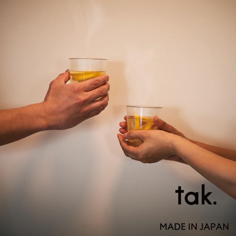 兩隻手各拿著一個透明玻璃杯，杯中盛有帶有檸檬片和淺黃色液體的飲品。杯口有細邊，杯身光滑。