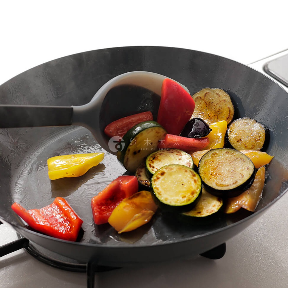 平底鍋中煎炒著各種切塊的蔬菜，有茄子、櫛瓜、甜椒，以及一旁的調理匙。