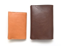 兩個職人手作皮革翻蓋記事本書套，一個為淺棕色，另一個為深棕色，皆為皮革材質，有縫線裝飾。