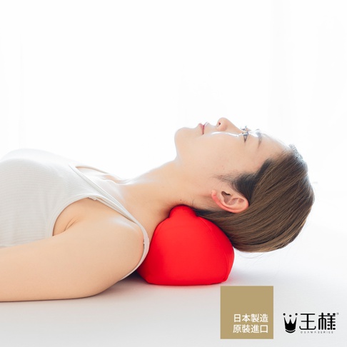 一位女性仰躺，頭部下方襯著一個紅色的指壓按摩枕，枕頭呈現圓潤的球狀，材質看起來柔軟。