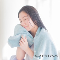 一位亞洲女性將一條淺藍色的毛巾輕輕貼在臉上，毛巾材質柔軟，有吸水效果。她閉著眼睛，面帶微笑。