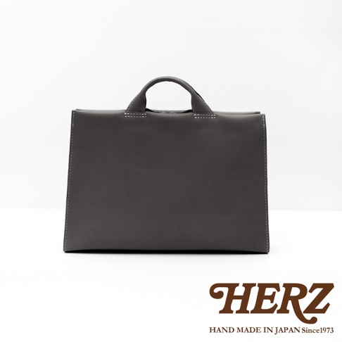 日本HERZ手工皮革簡約商務公事包，採用深灰色皮革製成，中間有白色縫線和手提帶。