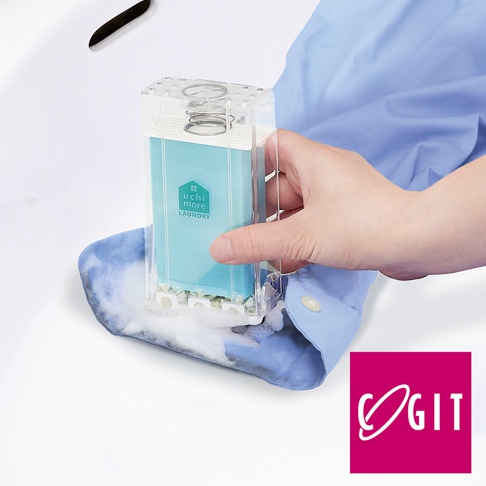 透明塑膠盒裝的淺藍色泡沫洗衣皂盒刷，盒內有彈簧和淺藍色皂液，手持洗衣皂盒刷在淺藍色襯衫上產生泡沫。