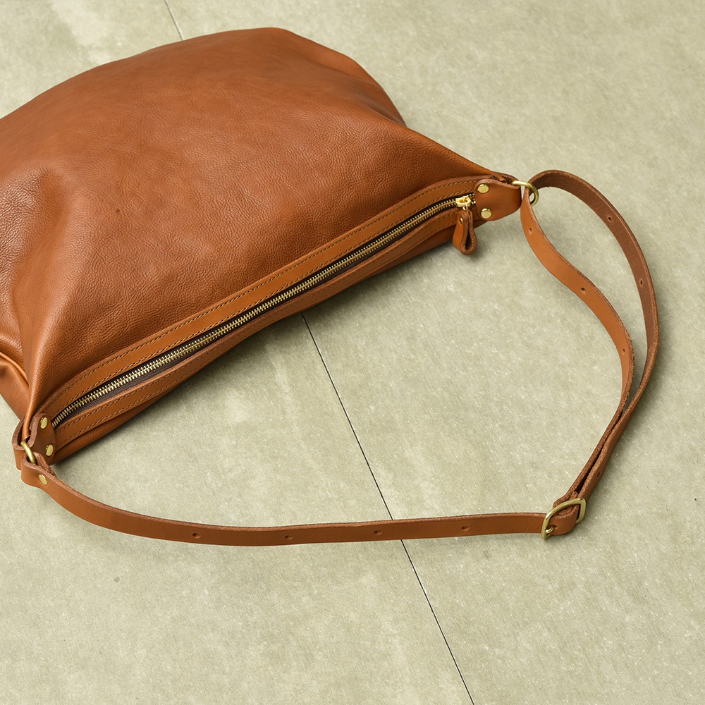 職人手作皮革Organ單肩半月包，採用柔軟的棕色皮革製成，搭配金色拉鍊和可調節的皮革肩帶，展現簡約的半月形設計。