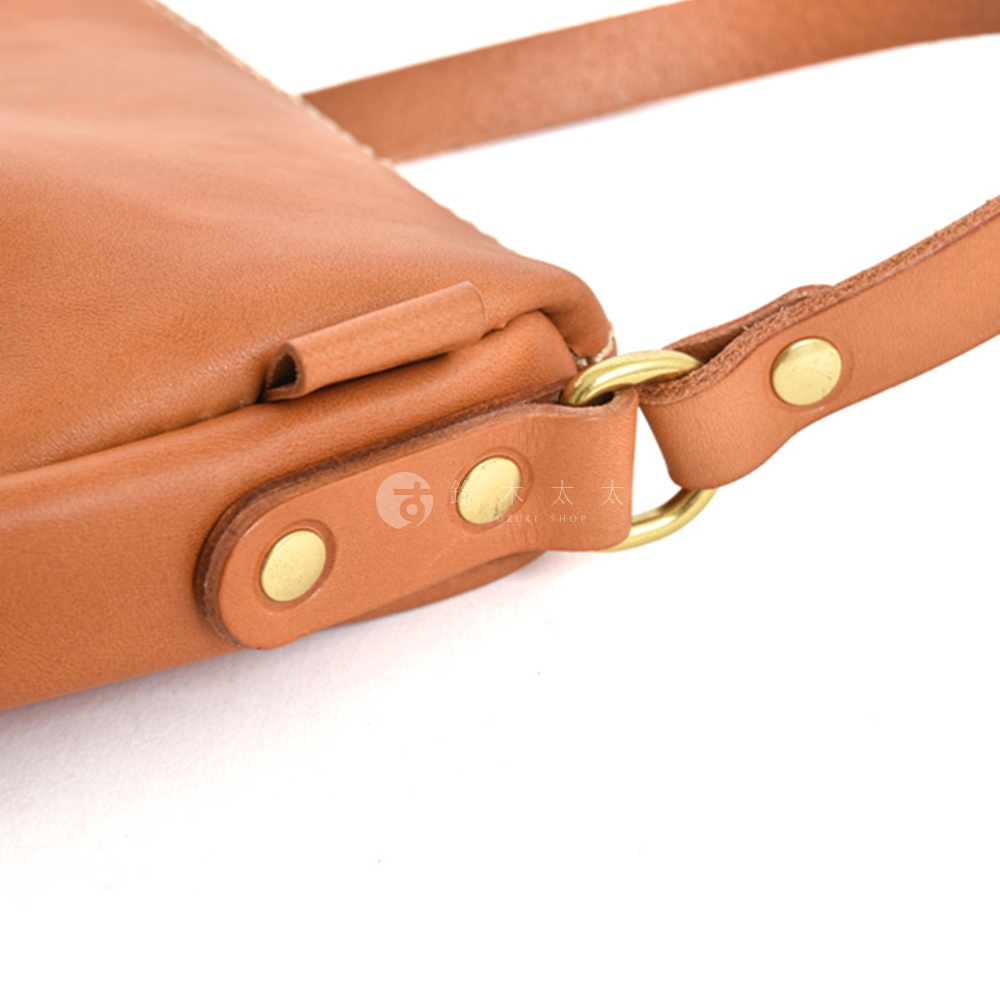 以職人手作皮革半圓馬鞍包的皮革細節，包含黃銅色的鉚釘和金屬環，展現精湛工藝。