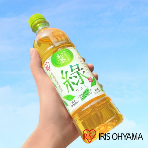 一隻手持著一瓶 IRIS OHYAMA 品牌的綠茶飲料，瓶身標籤上印有綠色的綠字與日文說明，背景為明亮的藍天白雲，呈現清新自然的情境。