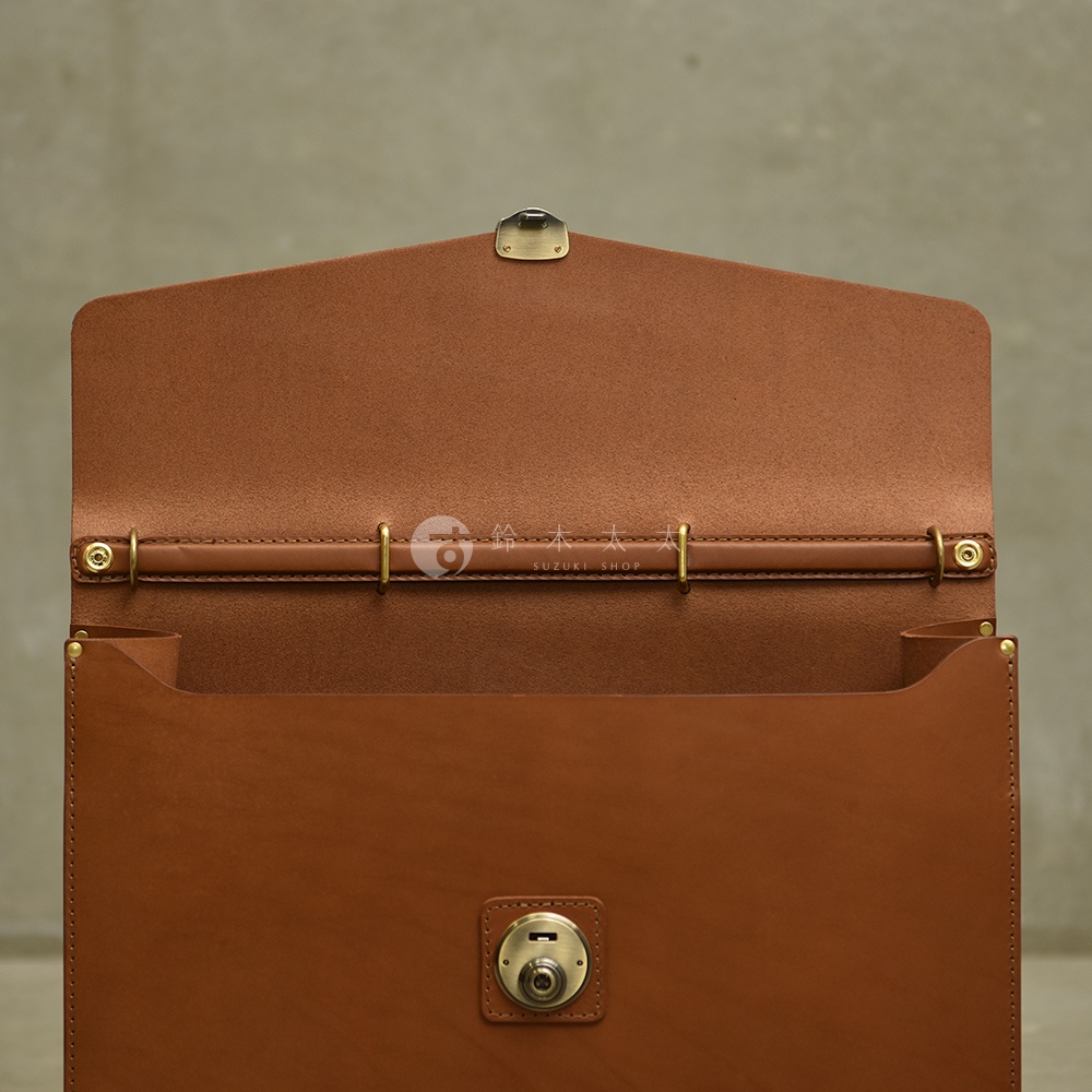 職人手作皮革Organ兩用商務公事包，呈現溫潤的棕褐色皮革，內裡為光滑皮革，外觀有金屬釦環與鎖扣，設計簡約大方。
