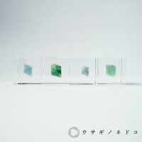 透明立方體內嵌四塊顏色從淺藍到翠綠的礦石，呈現不規則結晶狀。