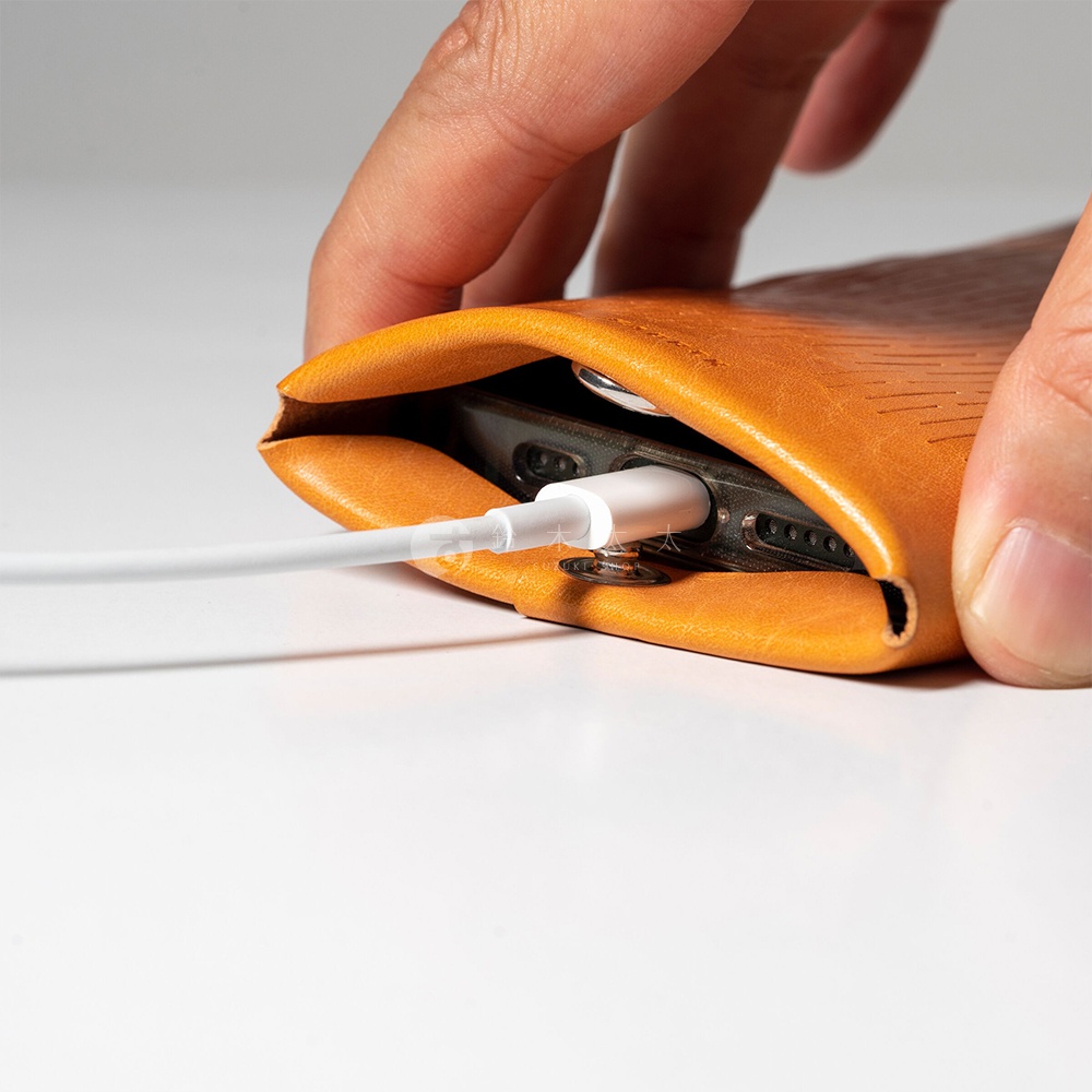 一位手指正在將一個棕色皮革手機套推入一個小包，手機充電線連接在手機上。