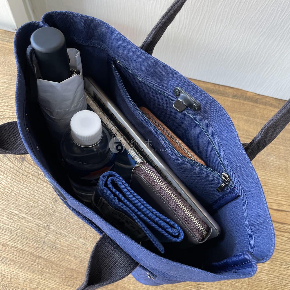 藍色帆布水桶托特包，內含雨傘、水瓶、筆記本、錢包和卡夾。包包內有拉鍊隔層及掛鉤，提把為黑色織帶。