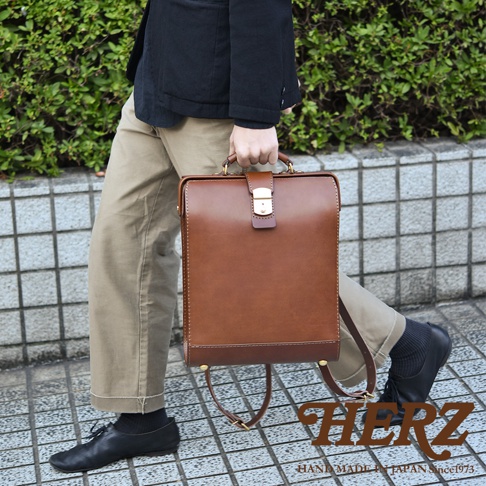 職人手作皮革杜勒斯商務後背包，經典棕色，採用厚實皮革製作，設計簡約，配有金色金屬鎖扣和提把，展現優雅質感，適合商務場合。