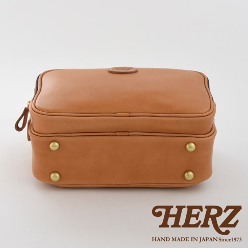 棕色皮革製成的方形公事包，頂部有拉鍊開口、皮革拉環及品牌壓紋圓形標誌，正面底部有兩顆黃銅色金屬釘。