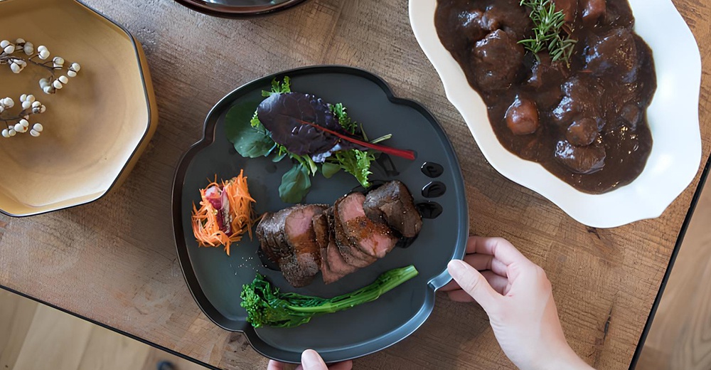 芥黃釉美濃燒八角盤，盤中盛有切片烤牛肉、蔬菜沙拉、炒紅蘿蔔絲及一根綠色蔬菜。另一側有白盤盛裝燉牛肉。