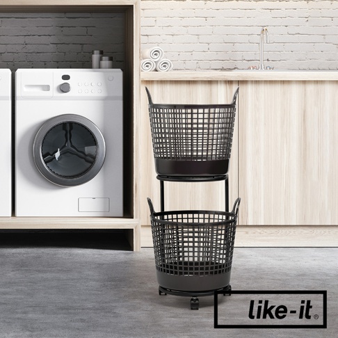 黑色的兩層式圓形洗衣提籃，由塑膠網格製成，帶有提把和輪子，放置於洗衣機旁。