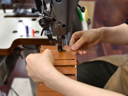 職人以縫紉機縫製淺棕色皮革多用途收納長夾，細節處可見縫線與皮革紋理。
