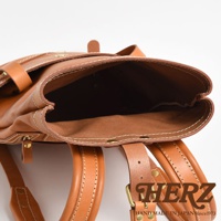 職人手作皮革雙口袋折蓋後背包，展示棕褐色調的皮革材質，帶有經典的白色縫線與金屬扣環，背包開口敞開，可見其內部結構。