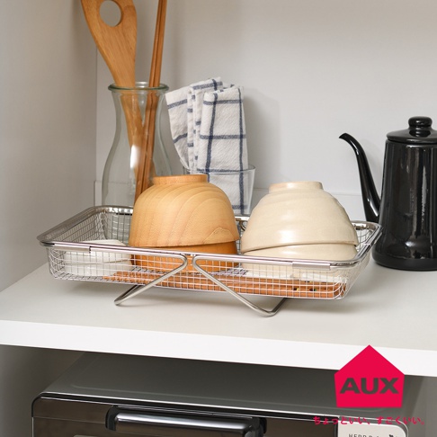 銀色金屬網狀伸縮瀝水籃，籃內有木碗、瓷碗及木筷，後方為玻璃瓶裝木筷、格子毛巾與黑色水壺。