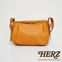 職人手作皮革復古翻蓋郵差包，採用溫暖的焦糖棕色皮革，搭配可調節的皮質背帶與銅質金屬扣。包身設計簡約，有著自然的皮革光澤與精緻的縫線細節。