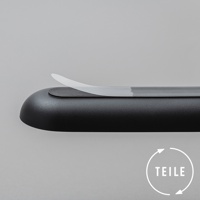 黑色圓潤的產品，表面有細微紋理，上方有一條半透明的白色薄片，部分區域有淺灰色液體痕跡。右下角有一個白色圓圈，內有箭頭循環符號和德語單詞「TEILE」。