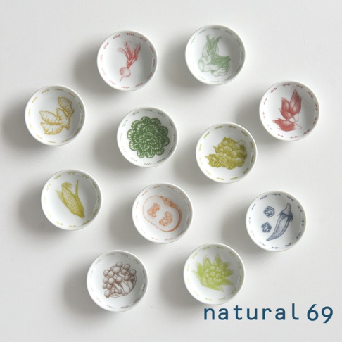 白色陶瓷迷你小菜碟，共五款，每款皆以手繪風格描繪不同蔬菜圖案，包括紅蘿蔔、青江菜、番茄、玉米、花椰菜、南瓜、秋葵、香菇等，色彩柔和，碟子邊緣有細緻的裝飾。