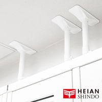 白色伸縮防傾桿，頂部有梯形固定墊，安裝於天花板與白色櫥櫃之間，展示了其支撐與固定功能。