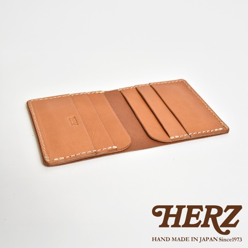 日本 HERZ 職人手作皮革二折式薄型卡片鈔票夾，以淺棕色皮革製成，露出內裡和卡槽細節，下方壓印品牌 LOGO 與 Handmade in Japan Since1973 字樣。