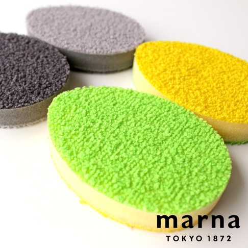 marna TOKYO 1872 品牌標誌旁有四塊橢圓形的菜瓜布，分別為灰色、炭灰色、黃色和綠色，其中綠色菜瓜布最靠近鏡頭