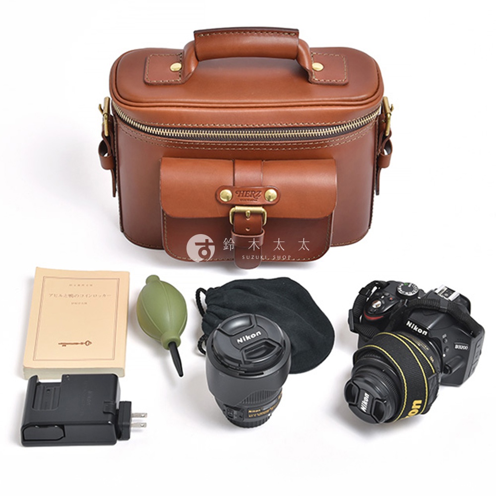 一個棕色皮革相機包，附帶一個前袋，以及相機、鏡頭、充電器、氣吹和一本小手冊。