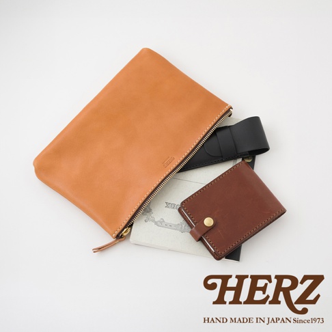 職人手作皮革長方形拉鍊收納包，展示了棕褐色皮革包、黑色皮革夾以及一個棕色皮革錢包，整體為簡潔的陳列。