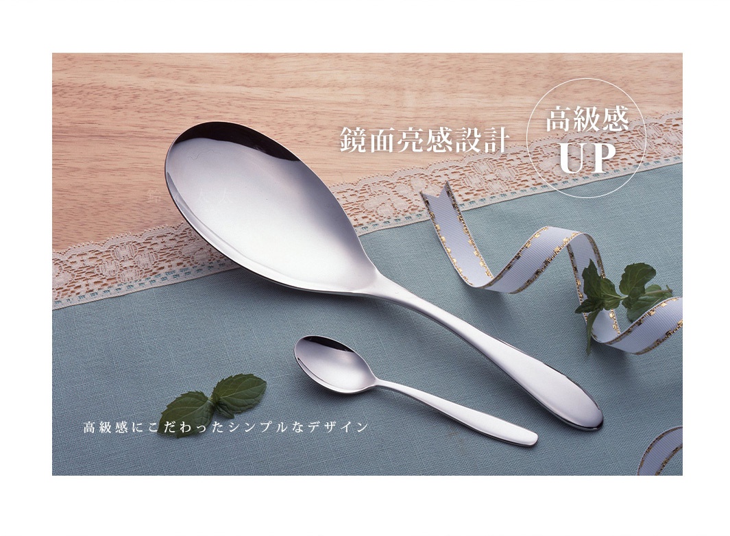 兩支不鏽鋼料理分食匙，一支較大，一支較小，均為銀色鏡面拋光。背景為木紋桌面和藍色布料，搭配蕾絲和裝飾緞帶。