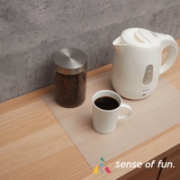 淺色半透明捲筒式砧板保潔墊片，置於木質檯面上，上面放有裝滿咖啡豆的玻璃罐、白色馬克杯及白色電熱水壺。