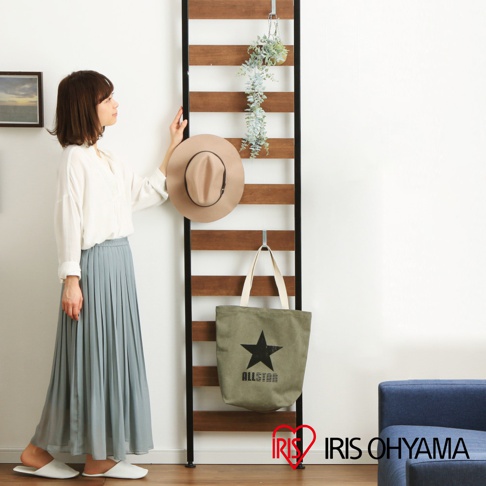 頂天立地收納掛架，黑色金屬框架，裝有橫向木紋層板，可掛置淺褐色圓頂帽和軍綠色帆布袋。