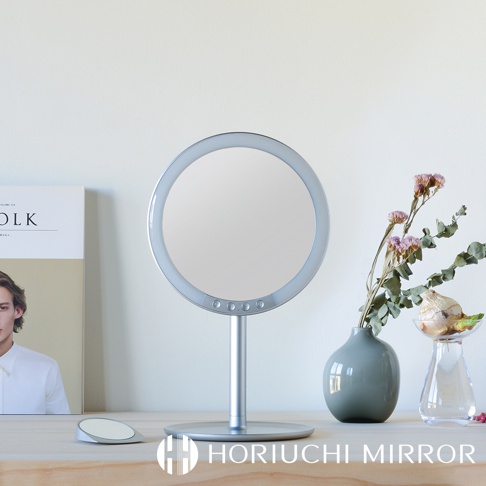 銀色圓形LED化妝鏡，鏡面周圍有圓形光環，底部設有觸控按鈕，鏡架和底座均為銀色金屬材質。