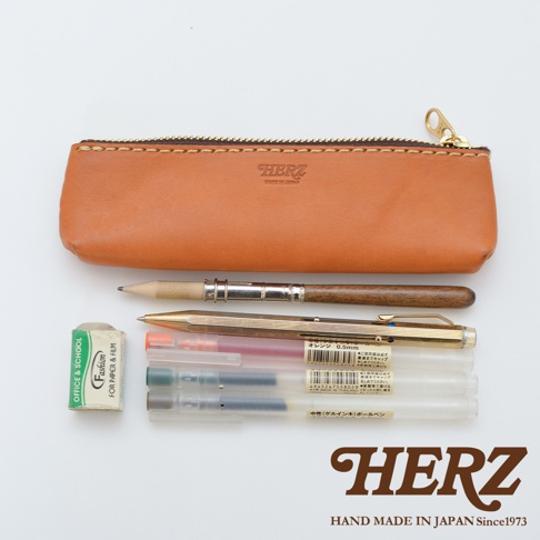 棕色皮革筆袋，內含一支木桿鉛筆、一支金色筆、一支紅色簽字筆、一支綠色簽字筆、兩支透明簽字筆，以及一塊寫著「OFFICE & SCHOOL FASHION FOR PAPER & FILM」的白色橡皮擦。