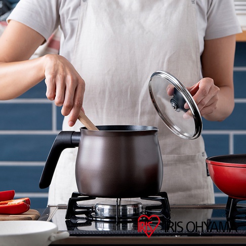 一只棕色鑽石不沾單柄小湯鍋，鍋蓋為透明玻璃材質，鍋柄為黑色，置於瓦斯爐上，有人手持木勺在鍋中攪拌。